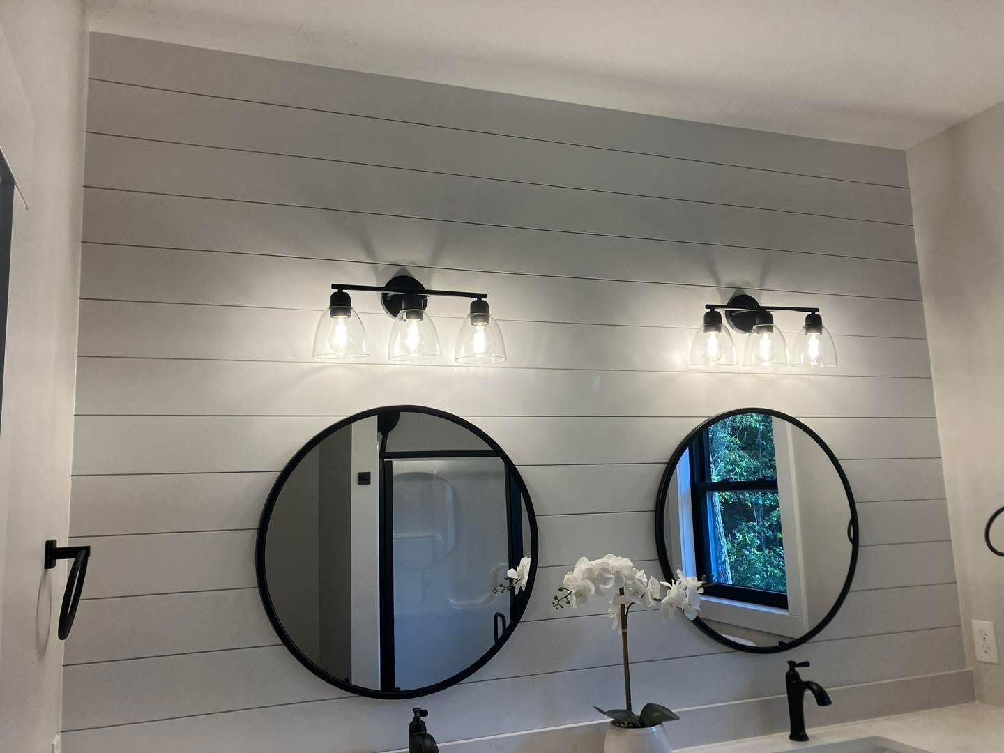 Bathroom with two round mirrors, black lights, white plank wall, and a white countertop.