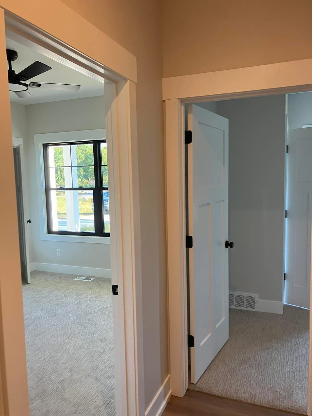 Hallway with two open doorways, light-colored walls and trim, carpet, and white doors with black hardware.