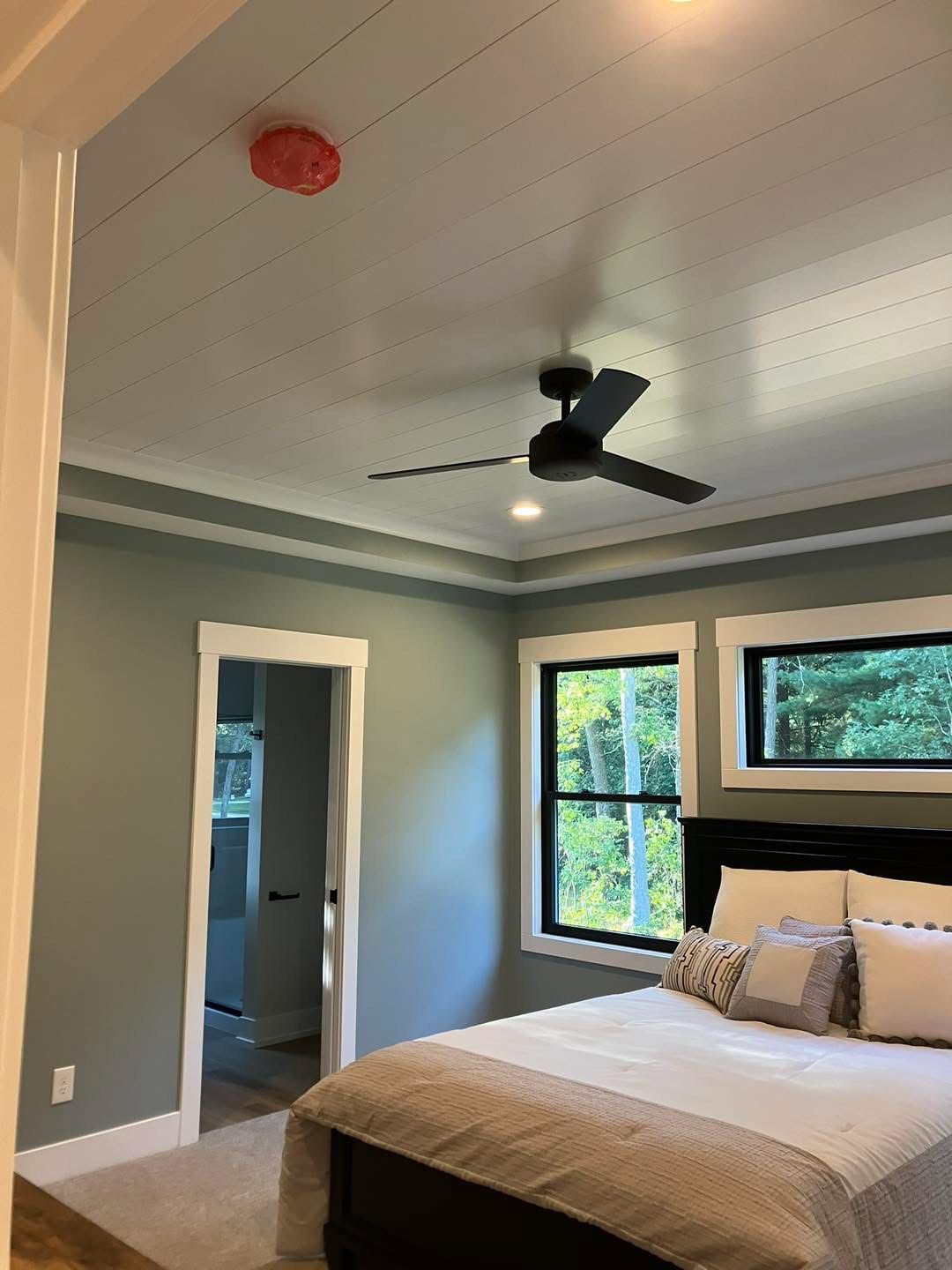 Bedroom with bed, windows, ceiling fan, smoke detector, and open doorway.