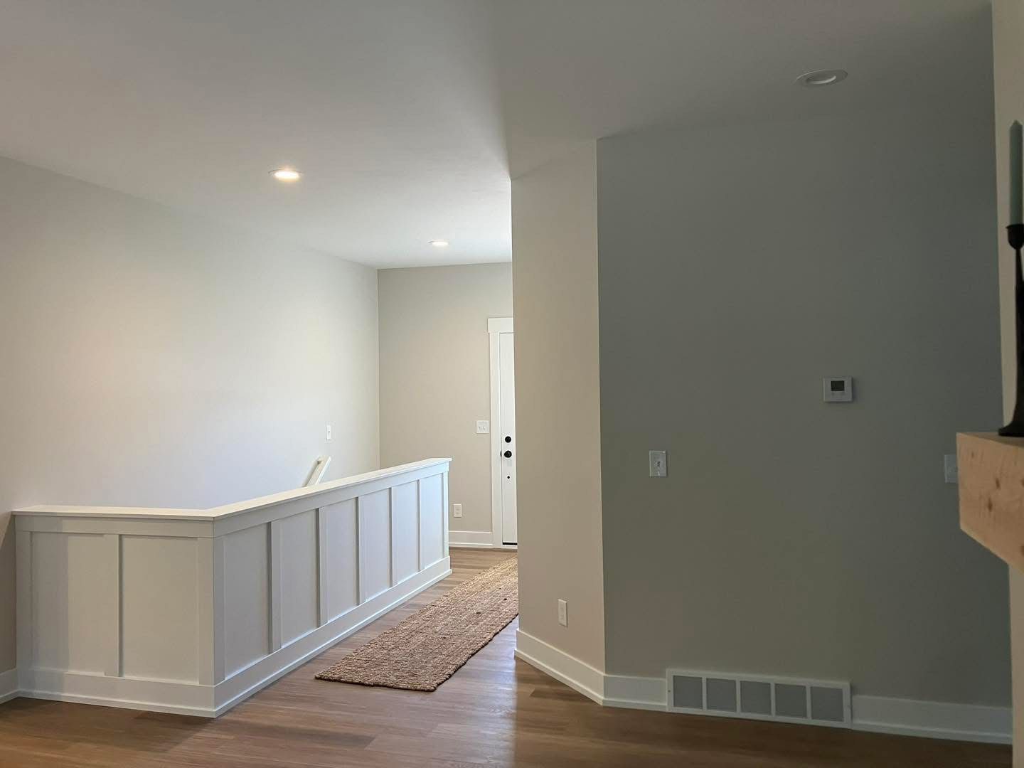 Interior hallway with white walls, wooden floors, and a white paneled railing.