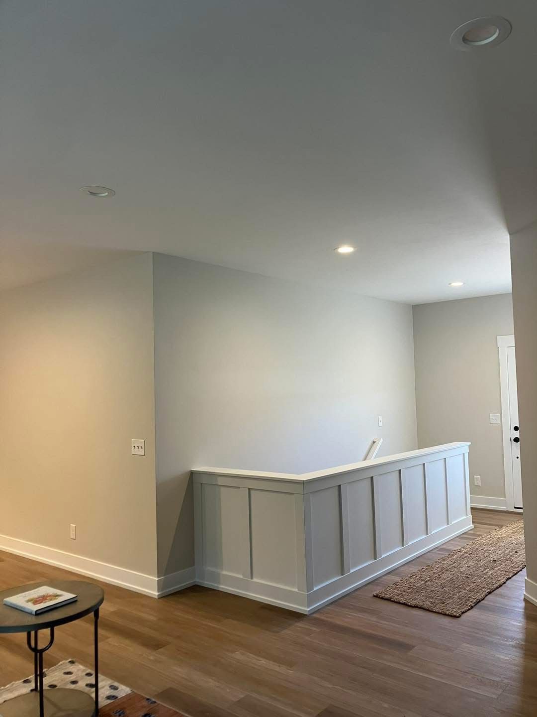 A light-filled interior with a white paneled half-wall, hardwood floors, and recessed lighting.