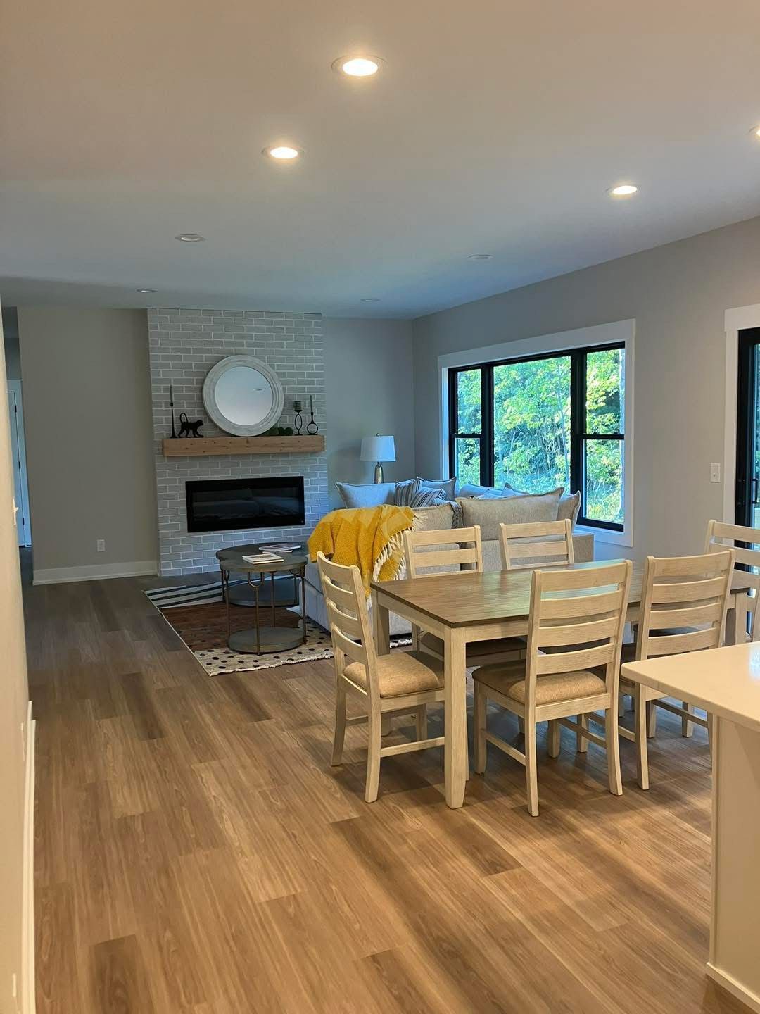 Living room with fireplace, dining area, light wood floors, and grey walls.