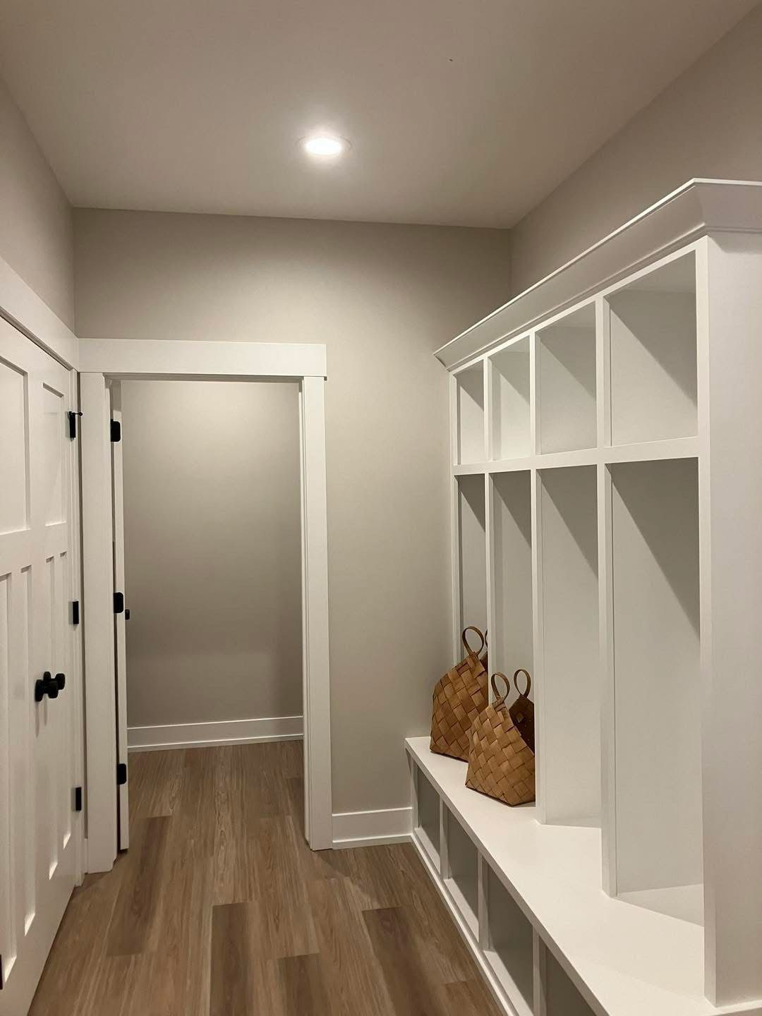 White built-in storage unit with cubbies and a bench in a hallway, next to a closed door.