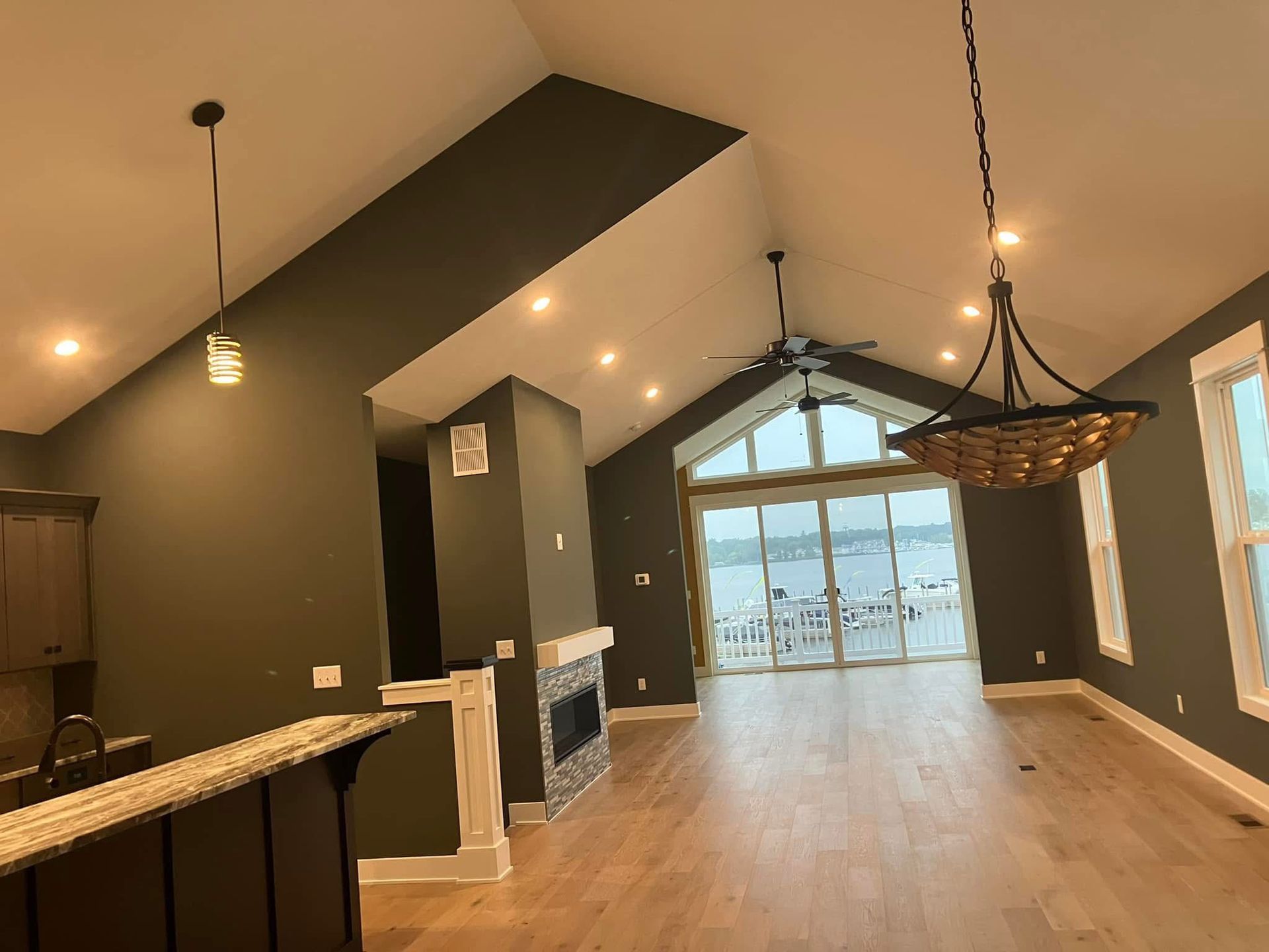 Interior of a modern home with dark green walls, wood floors, large windows overlooking water.