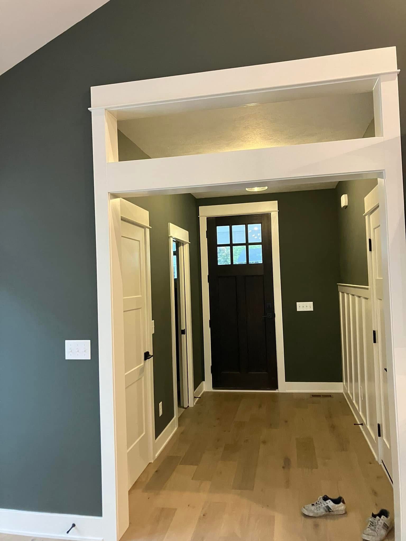 Hallway with green walls, white trim, wood floor, dark brown door at end.