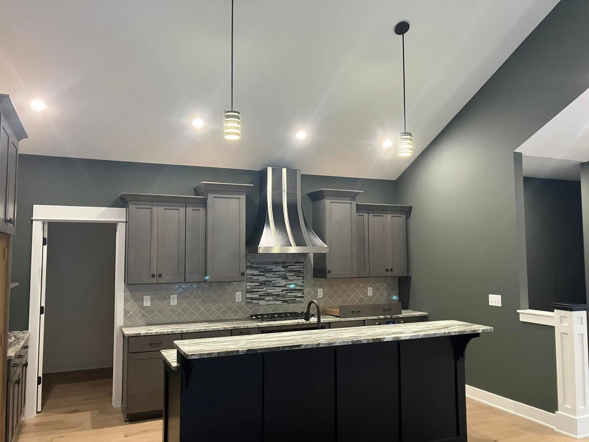 Kitchen with gray cabinets, black island, stainless steel hood, and pendant lights.