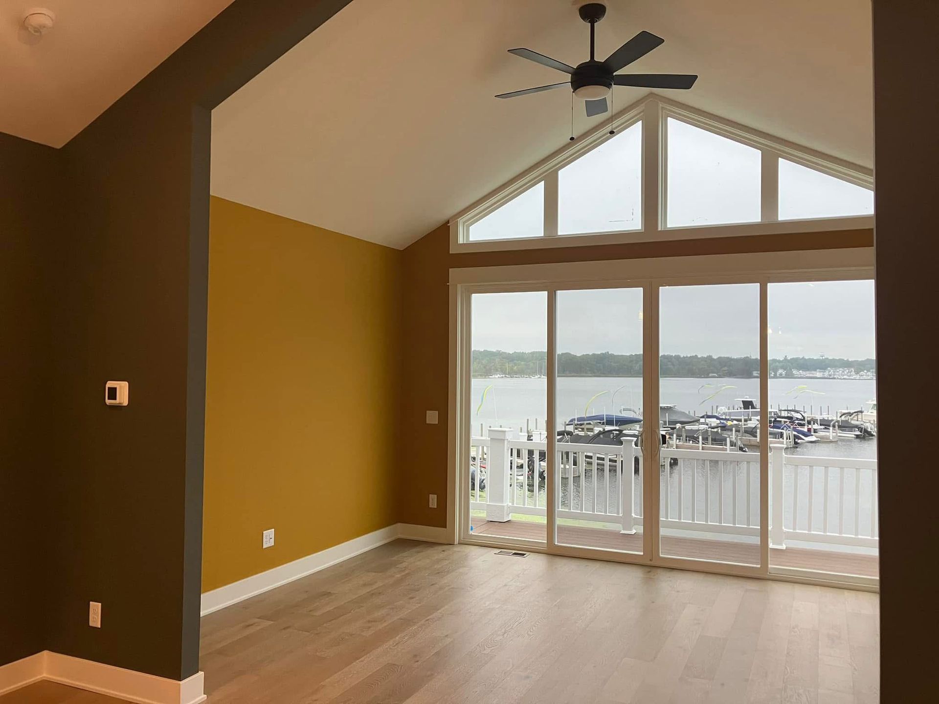 An empty room with a water view. Features large windows, a ceiling fan, and golden walls.