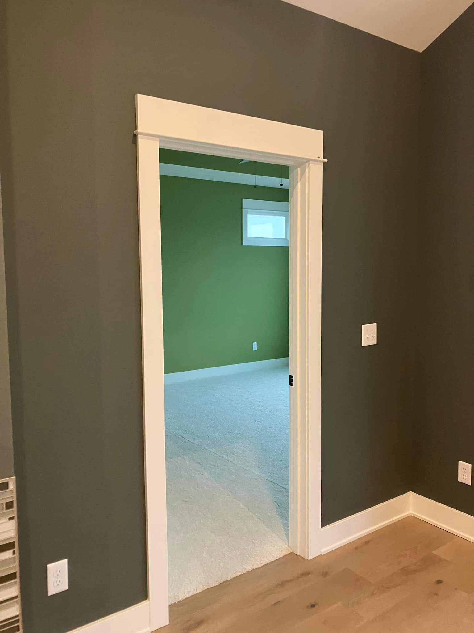 Doorway with white trim on gray wall, leading to a green room with a window.