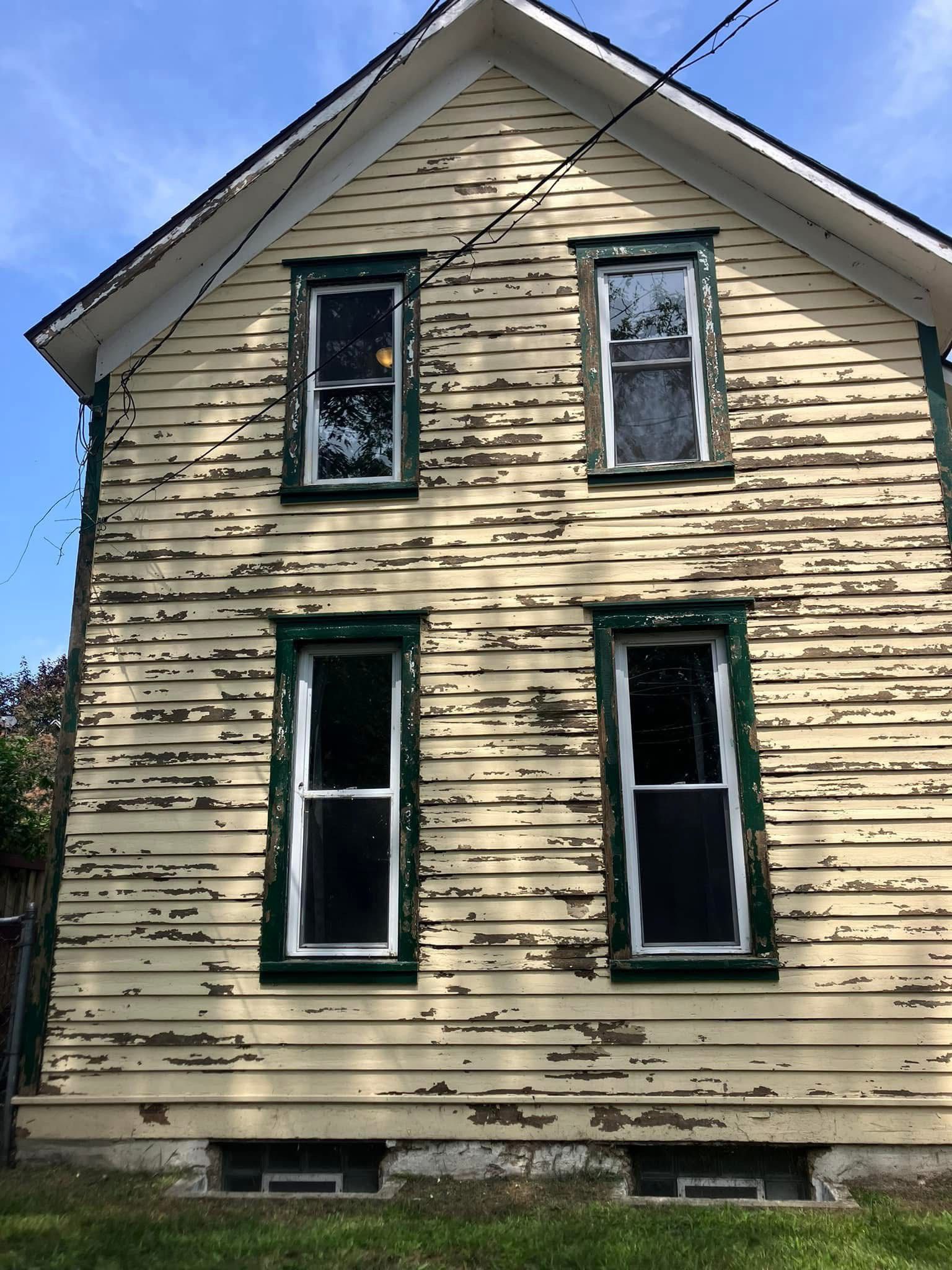 Two-story house with peeling yellow paint, green trim, four windows, and a basement.