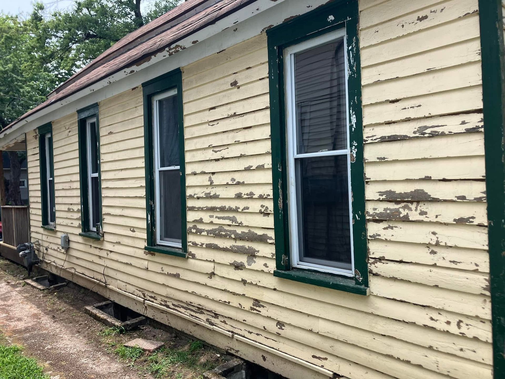 Yellow house with peeling paint, green trim around windows.