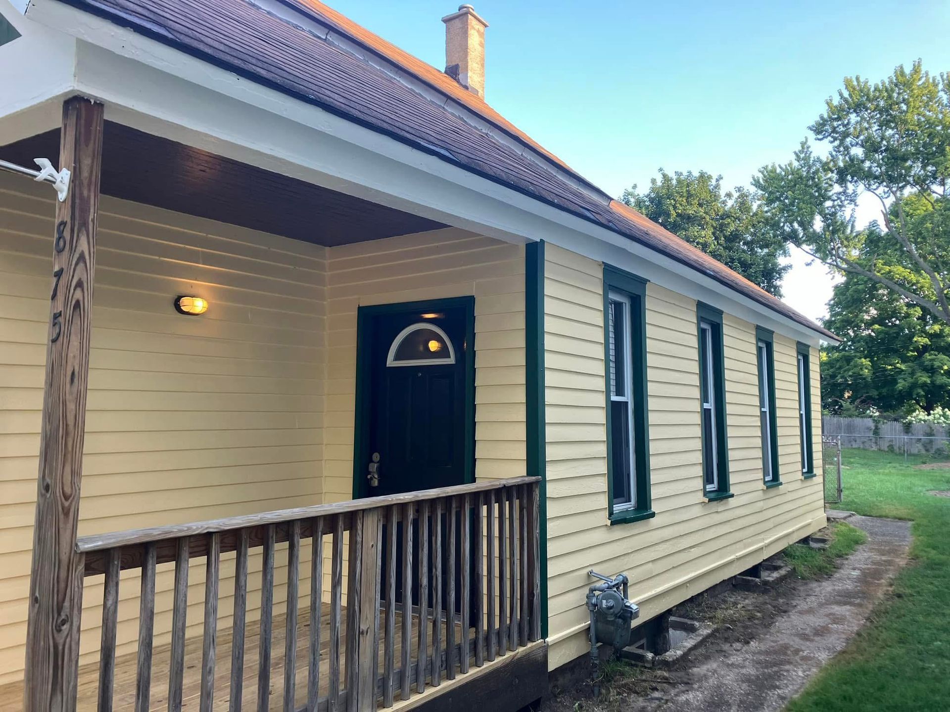 Yellow house with porch, dark door, green trim.