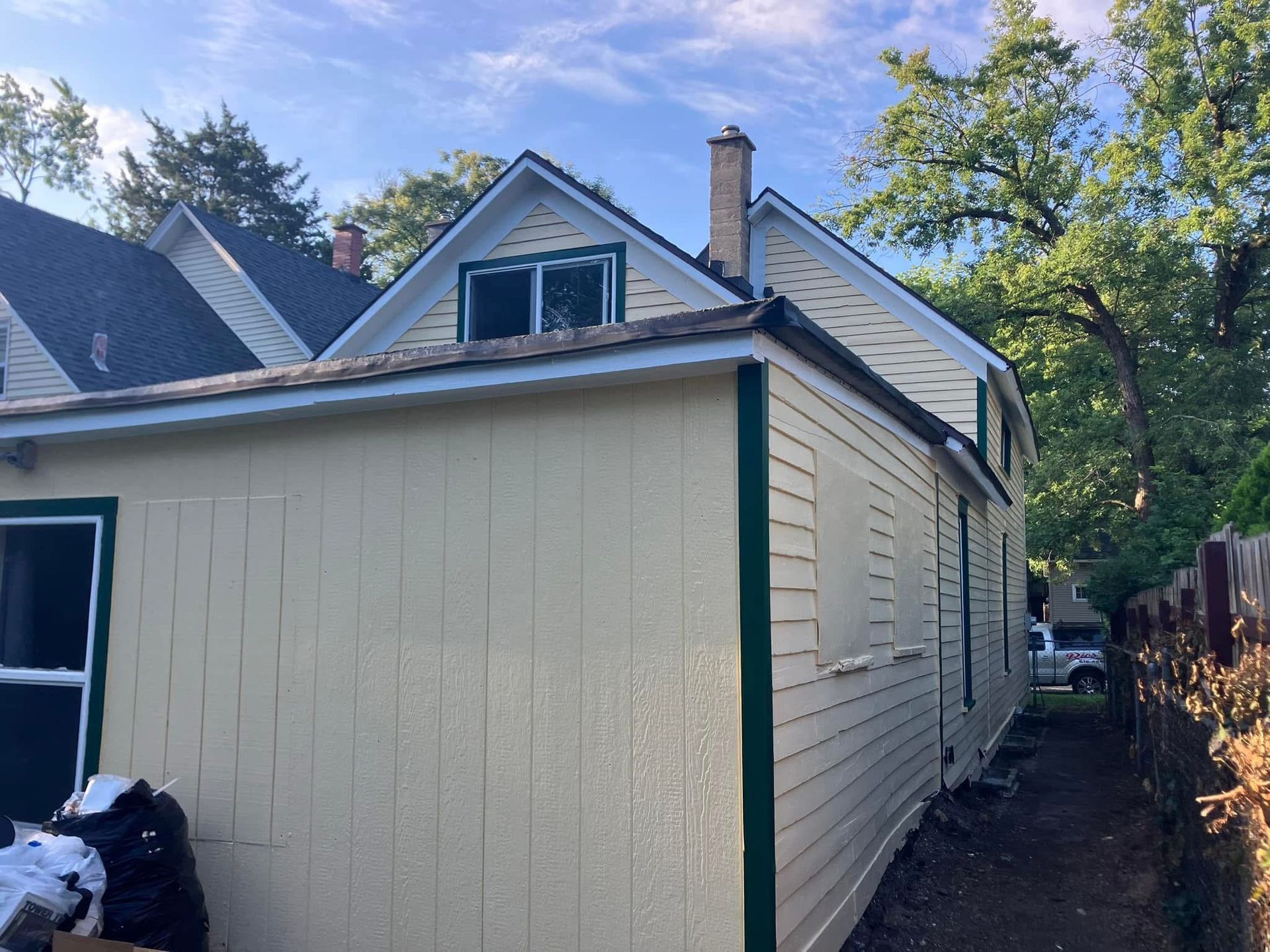 Yellow house with dark green trim, and a black roof on a sunny day.