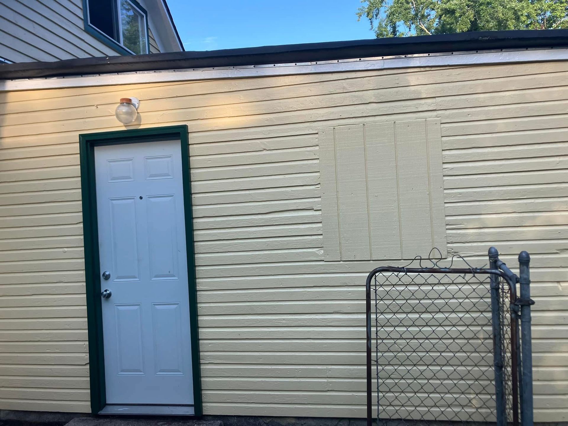 Yellow building with white door, green trim, and a small gated area.