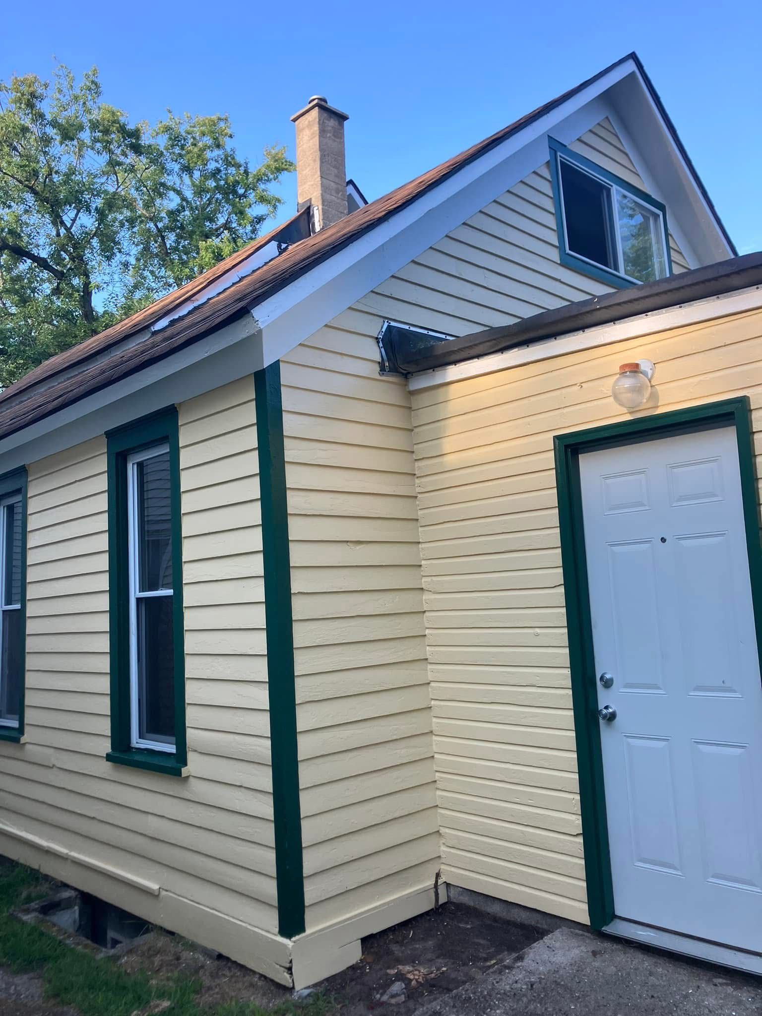 Yellow house with green trim, white door, and dark windows. Chimney on the roof.