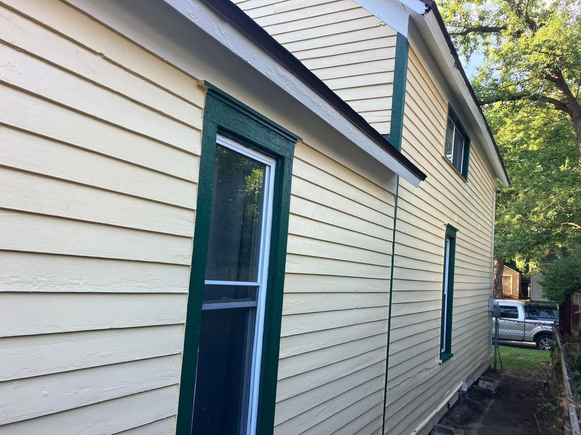 Side of a light yellow house with green trim and windows; sunny day.