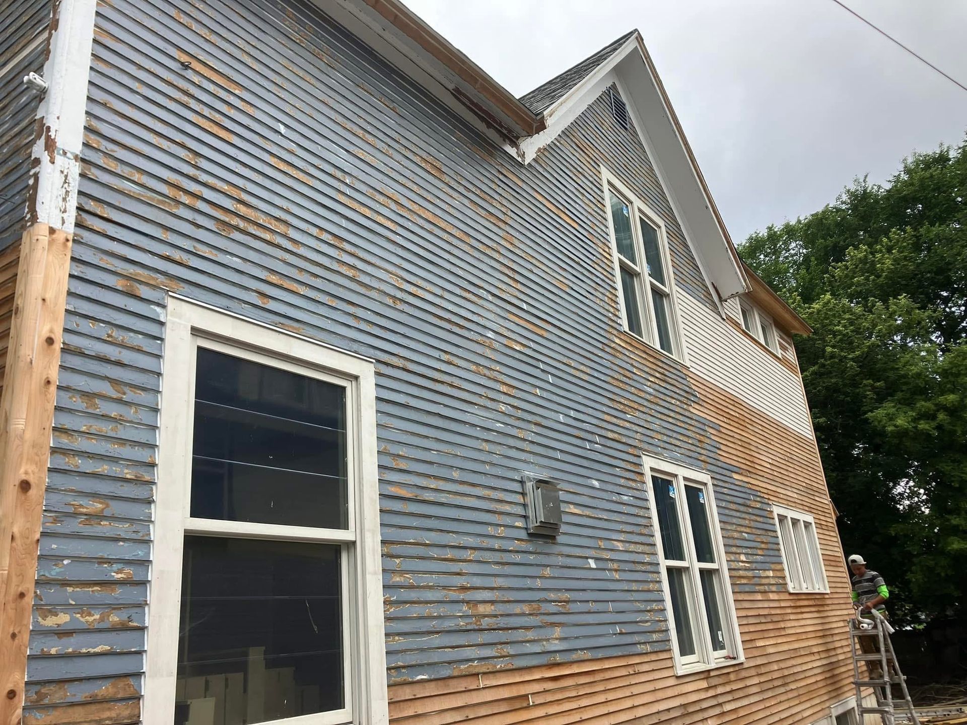 Two-story house under renovation with peeling blue siding and white-framed windows.
