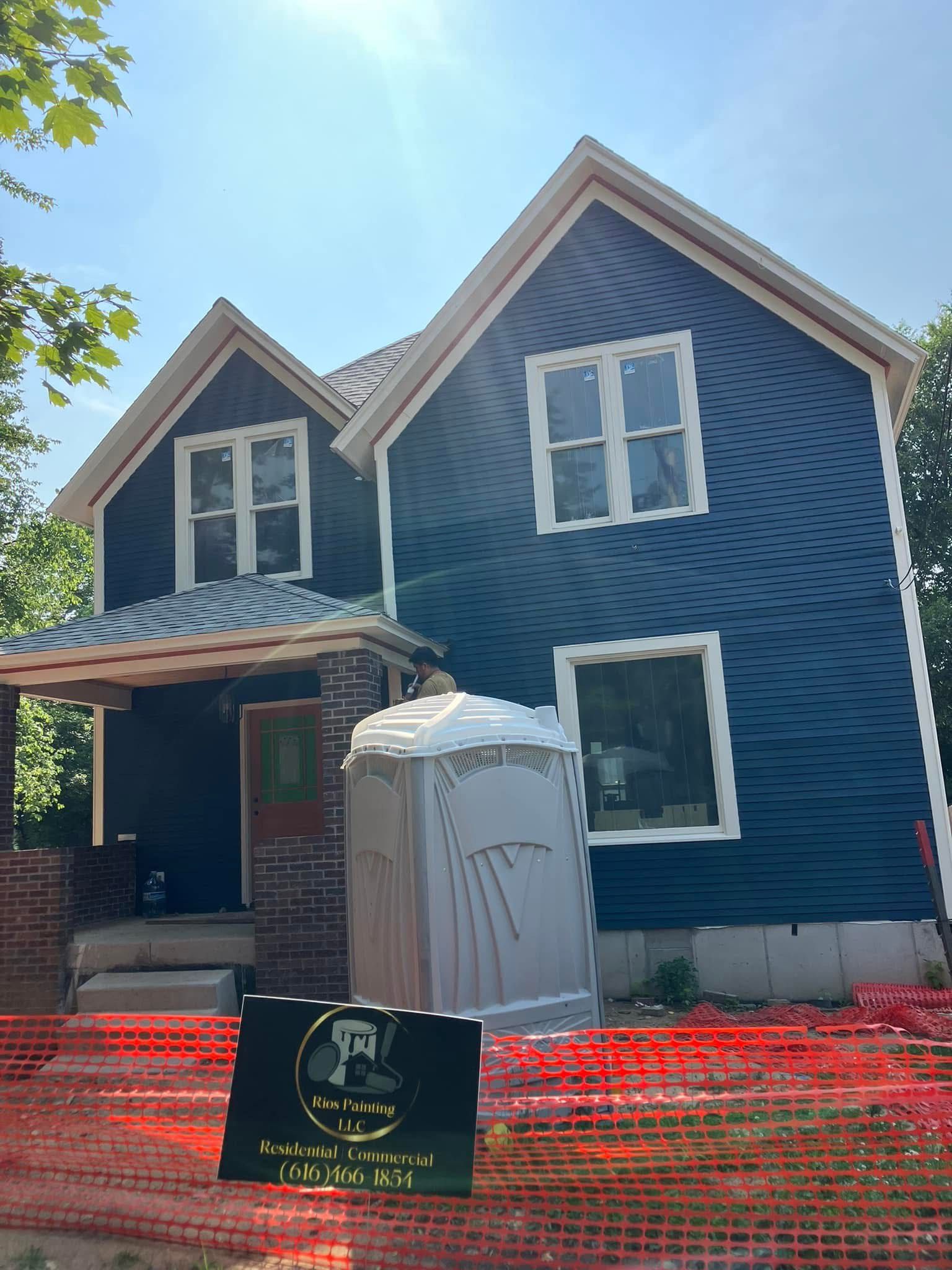 Blue house with white trim, construction site with portable toilet and orange barrier.
