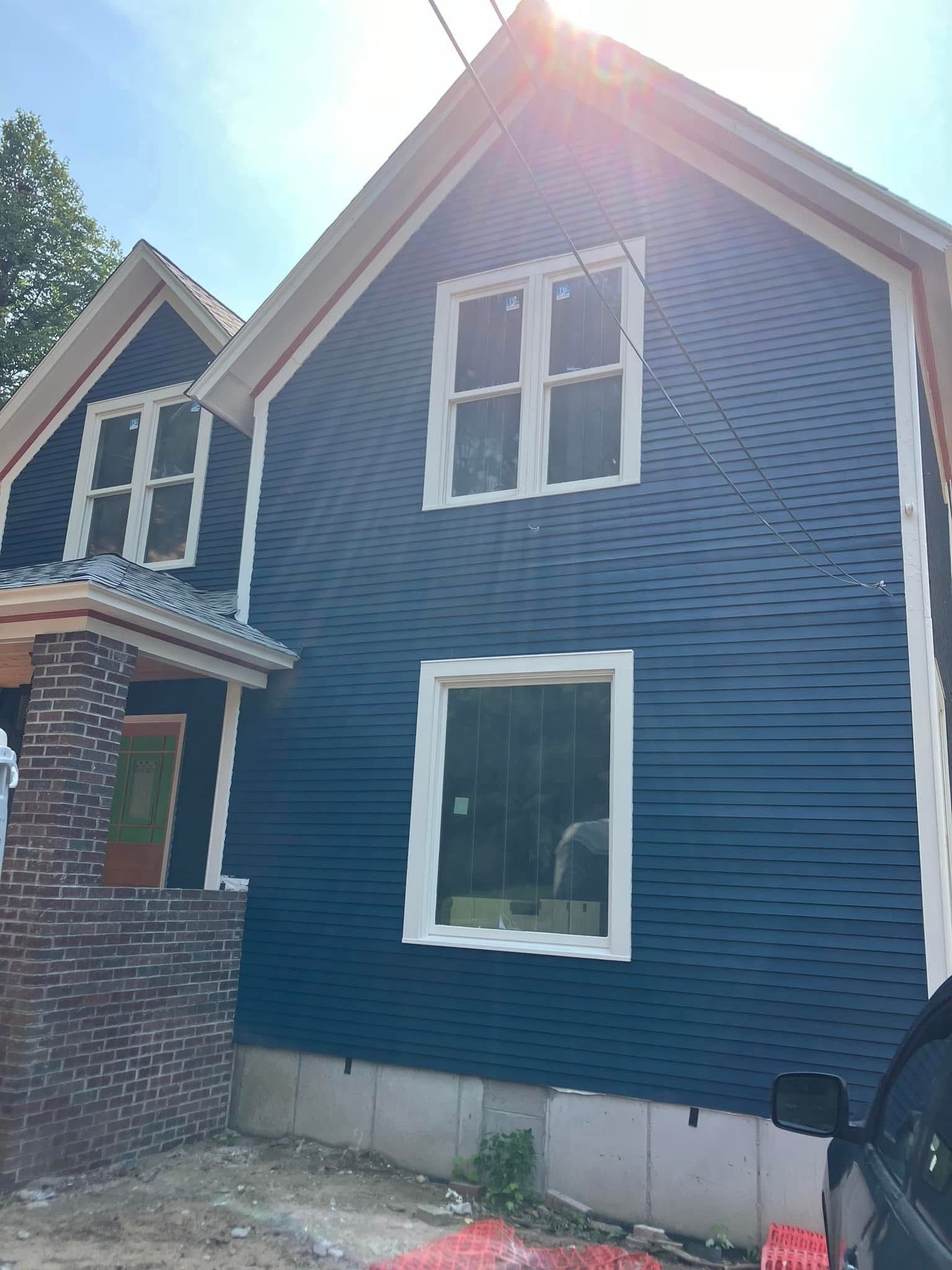Blue house with white trim and windows; brick foundation, sunny day.