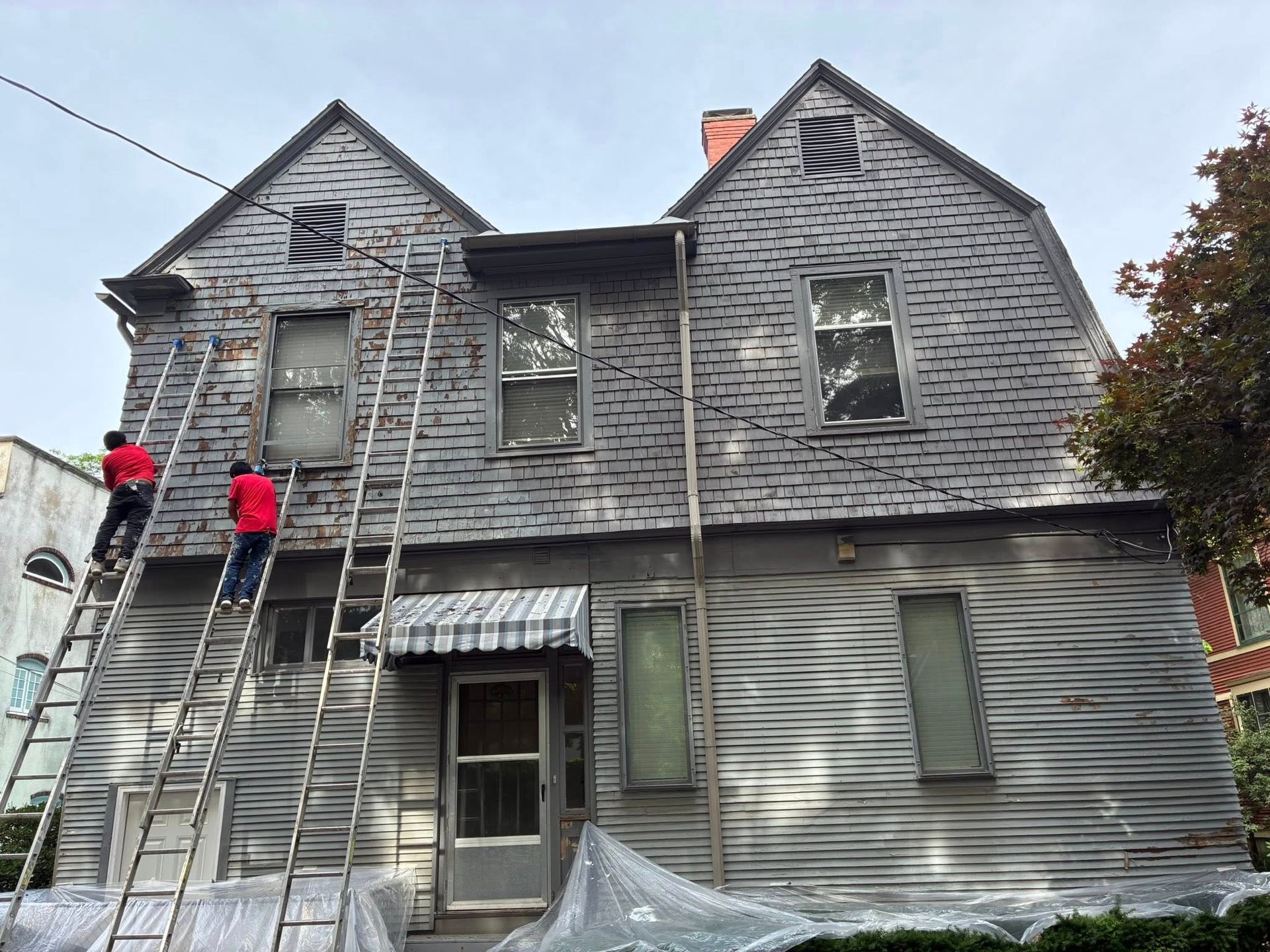 Two men are standing on ladders in front of a large brick building.