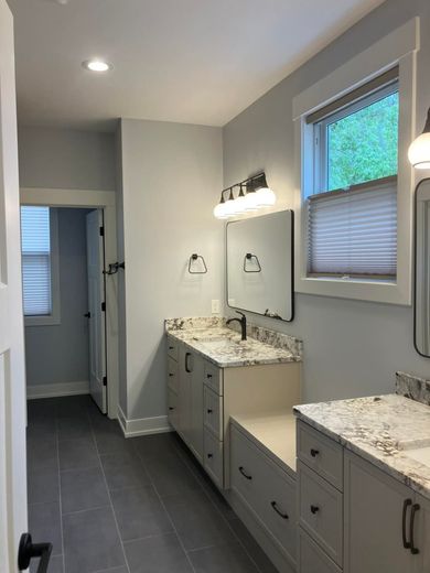 Bathroom with gray walls, cabinets, and floor. Granite countertops, a mirror, and a window are visible.