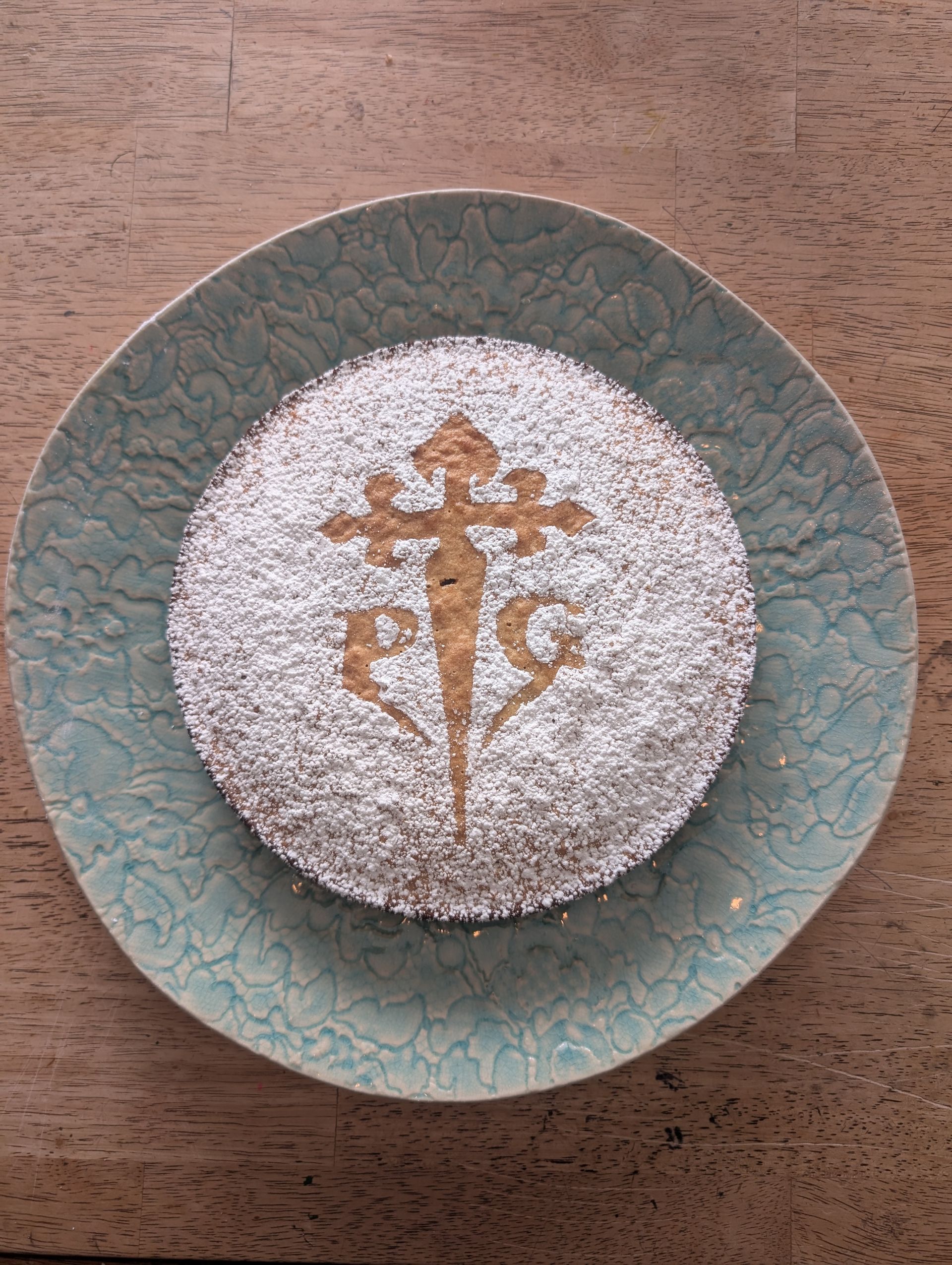 Tarta de Santiago cake dusted with powdered sugar, decorated with the Santiago cross, on a blue plate.