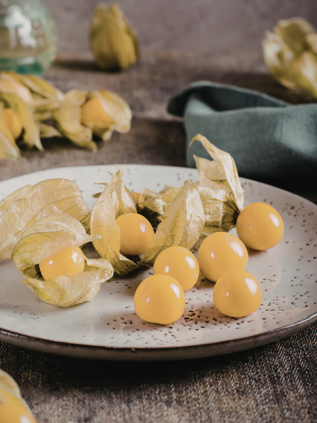 Golden cape gooseberries on a white plate, with papery husks, against a rustic backdrop.