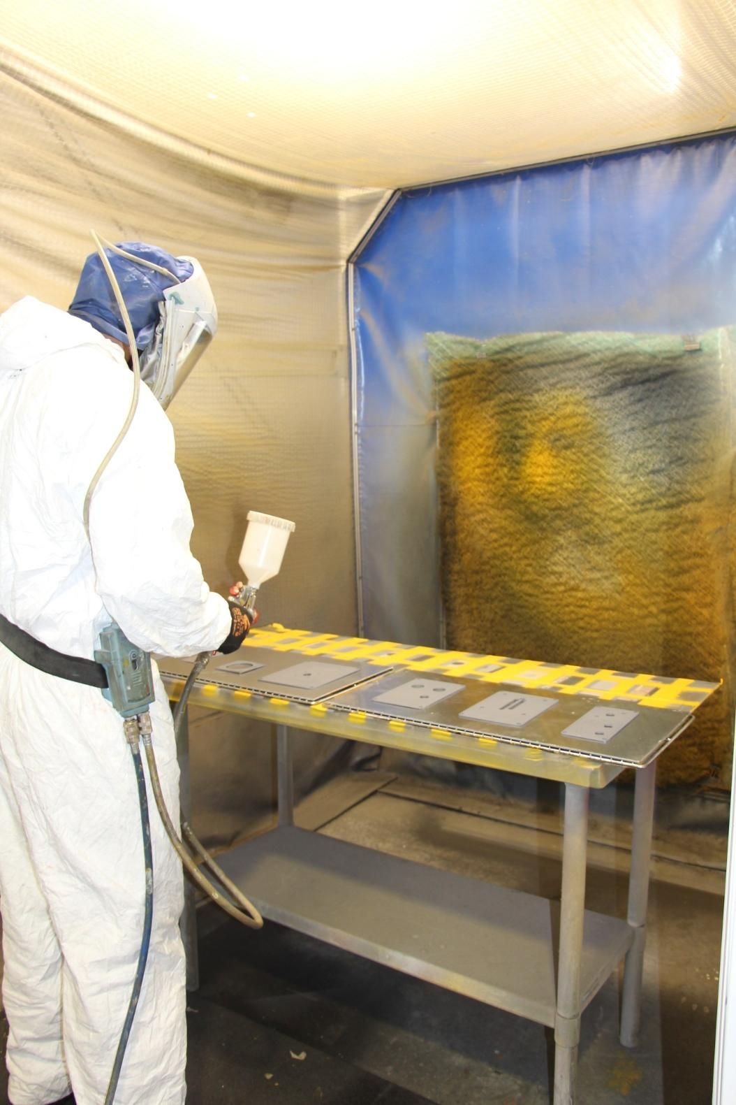 A Man in a Protective Suit is Spray Painting a Table — Total Engraving In Sandgate, NSW