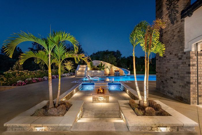 A large swimming pool is surrounded by palm trees and a fire pit.