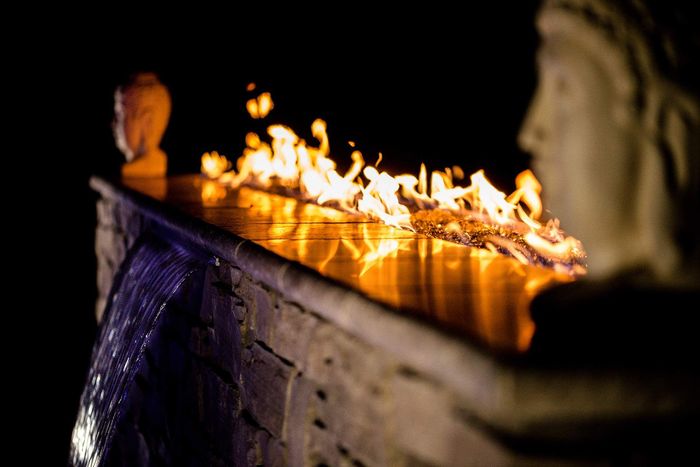 A fire pit with a waterfall and a statue in the background.