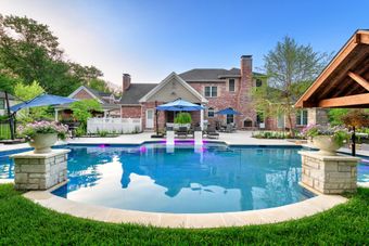 A large swimming pool in front of a large brick house.