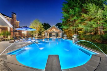 A large swimming pool is lit up at night in front of a house.