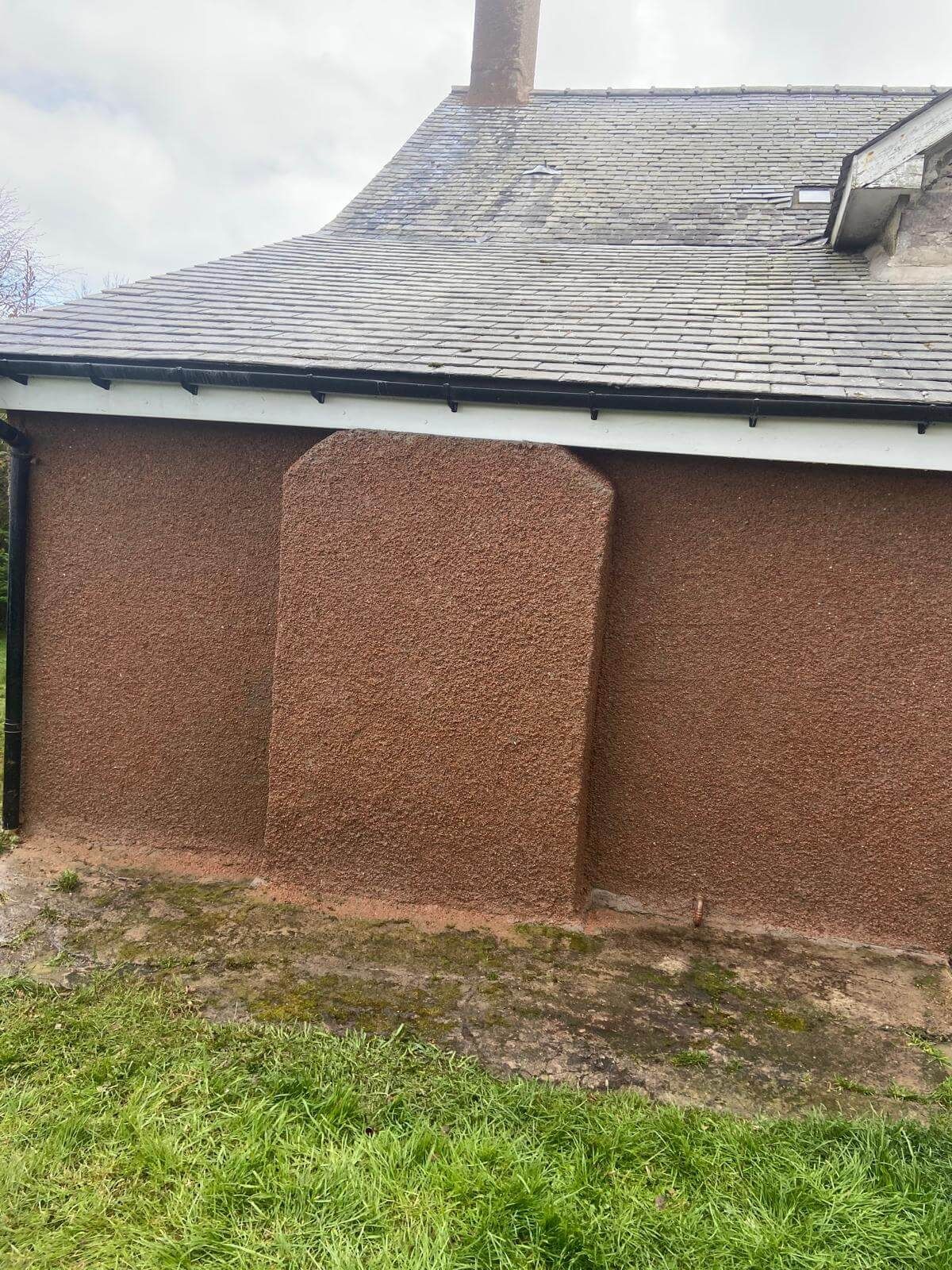 Brown stucco exterior of a building with a chimney. Gray roof and green grass in the foreground.