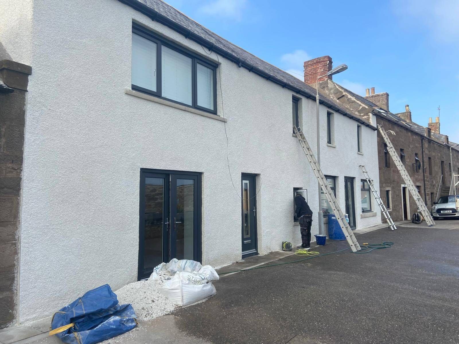 Row of houses being worked on, ladders propped against the walls. A person is working on the exterior of one house.