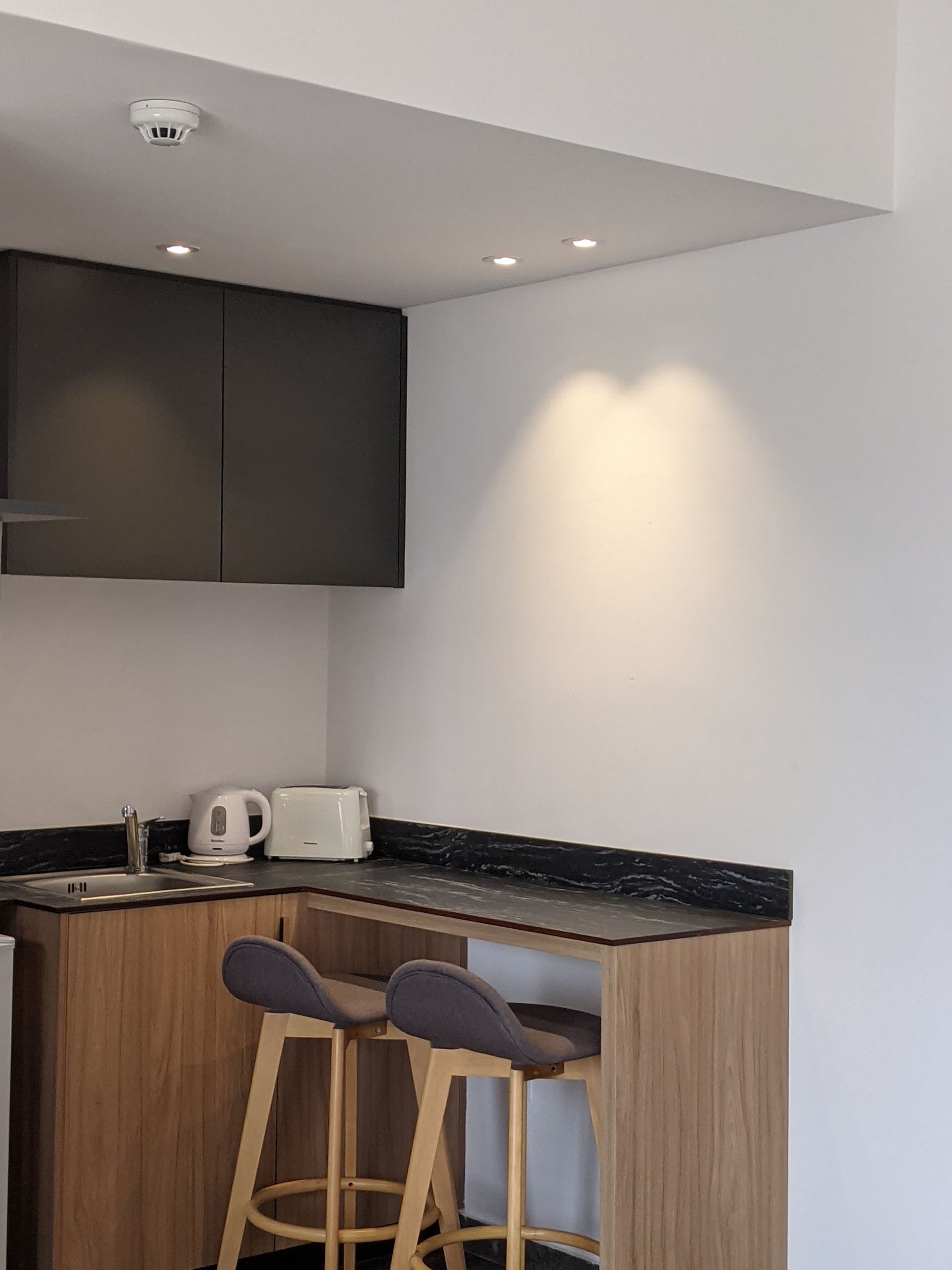 Small kitchen corner with a wooden counter, dark cabinets, and two bar stools.