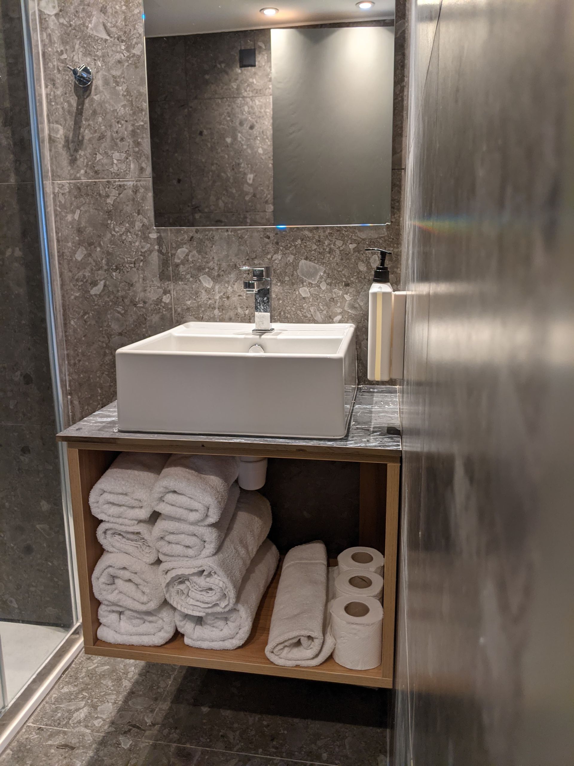 A bathroom with a sink , mirror , towels and toilet paper.