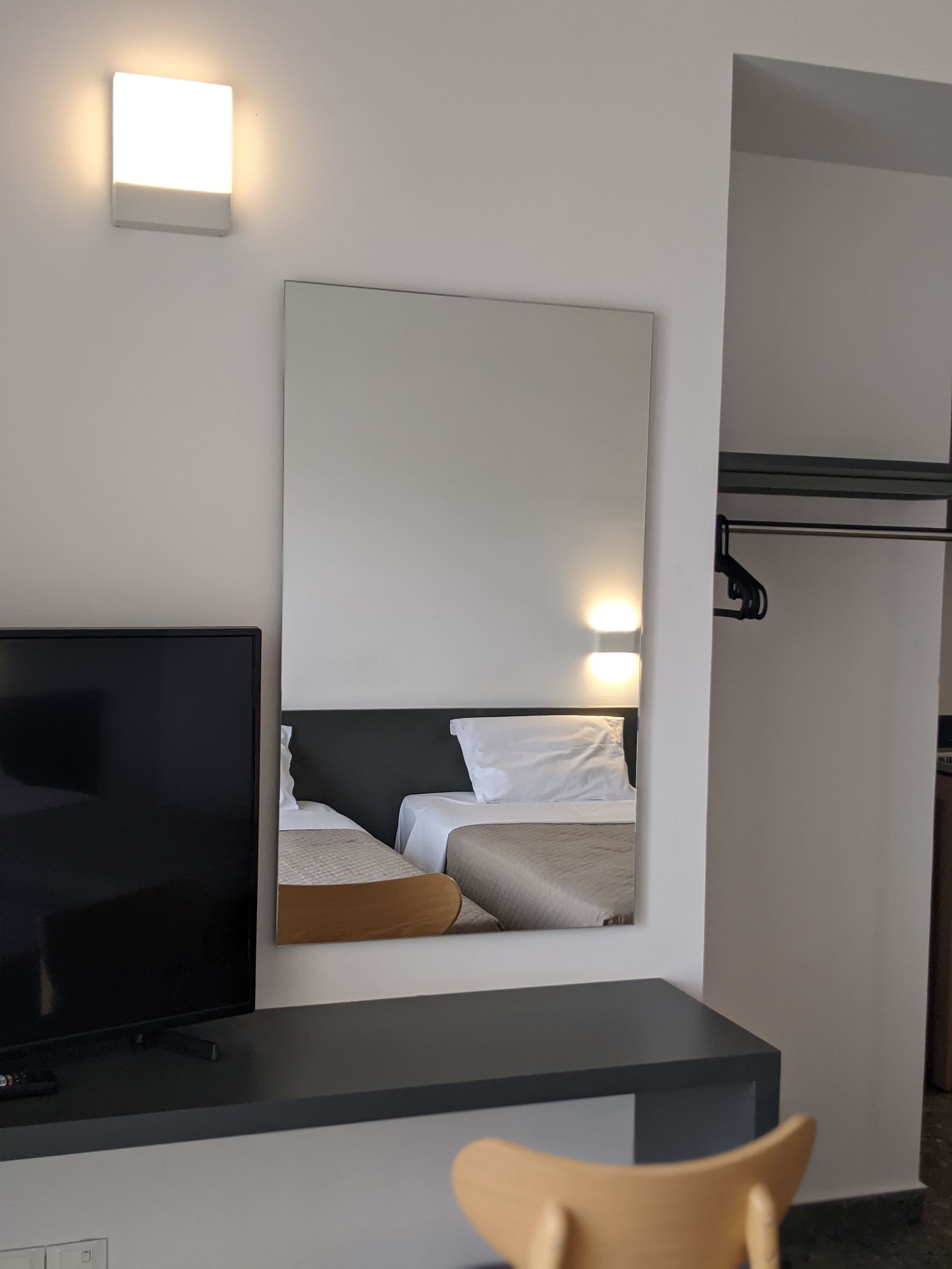 Mirror reflecting a hotel room with a bed. A desk with a TV and a chair are visible.