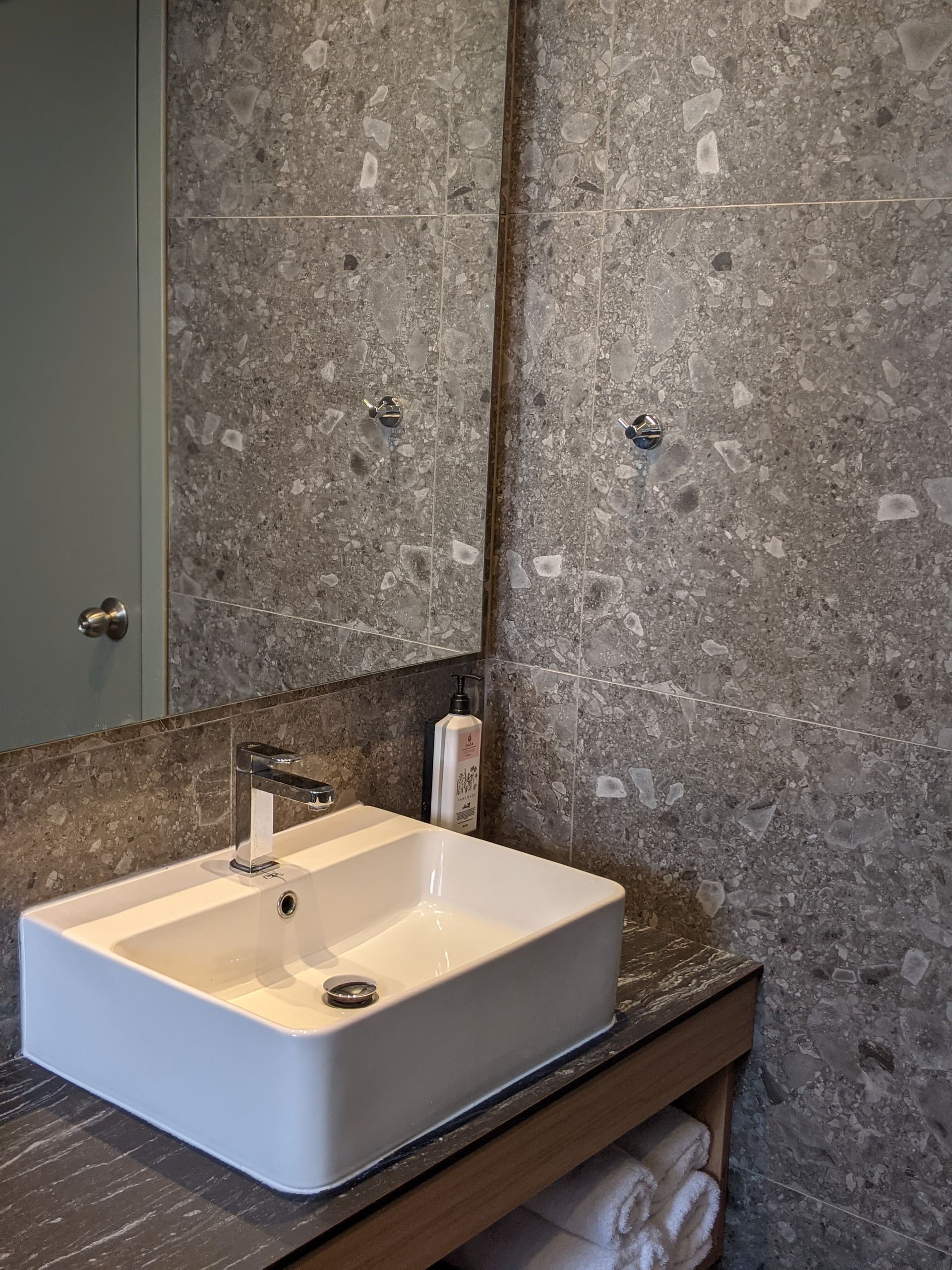 Modern bathroom with a rectangular white sink, gray speckled tiled walls, and a mirror.
