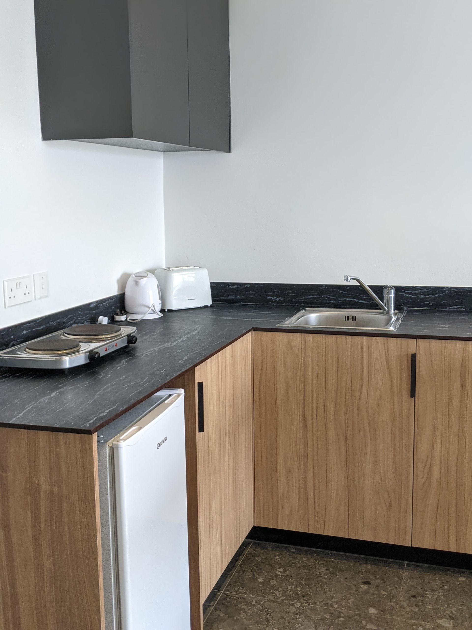 Small kitchen with light brown cabinets, black countertop, and a white refrigerator.