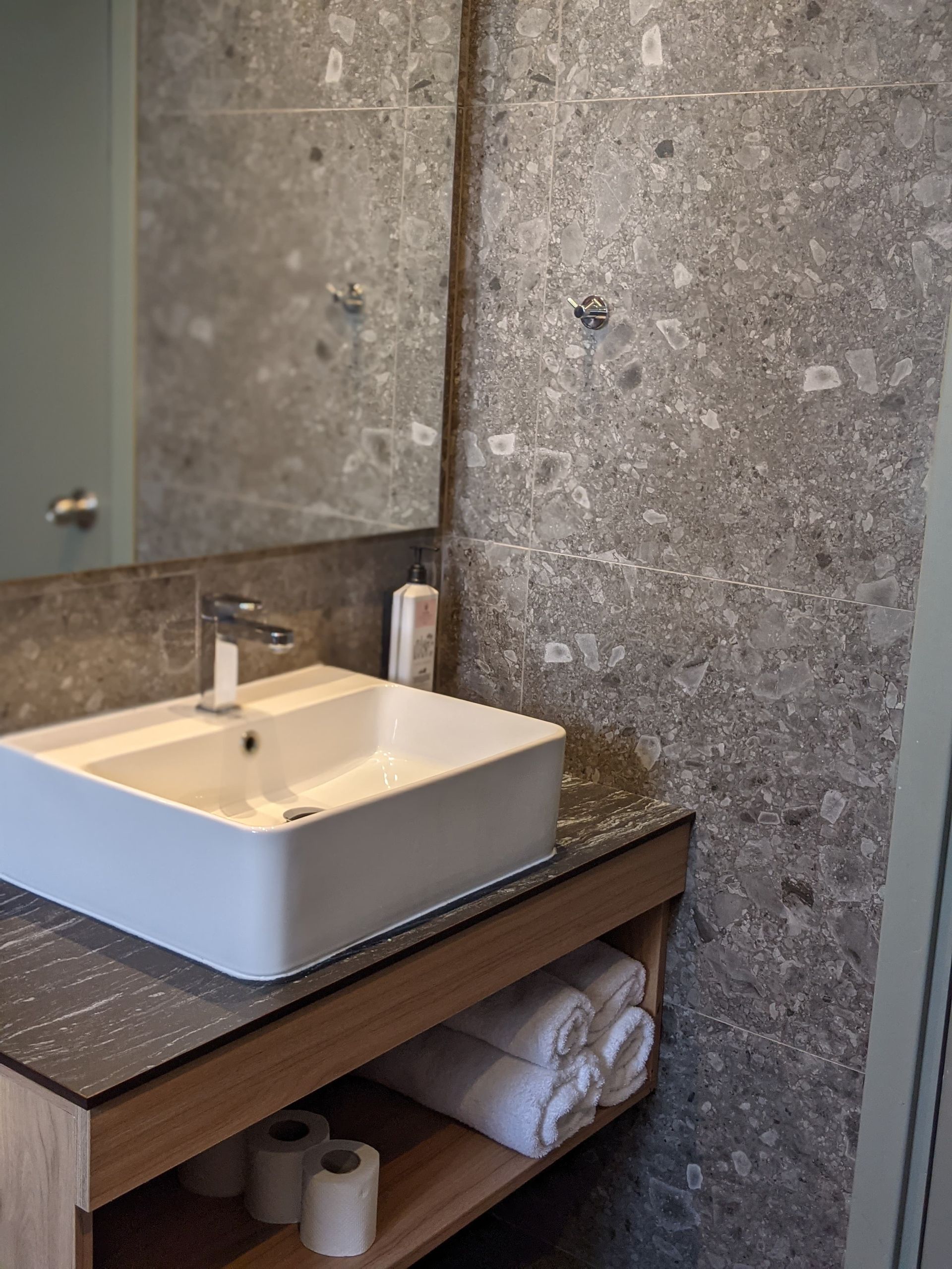 Bathroom vanity with a rectangular sink, mirror, and gray textured tile. 