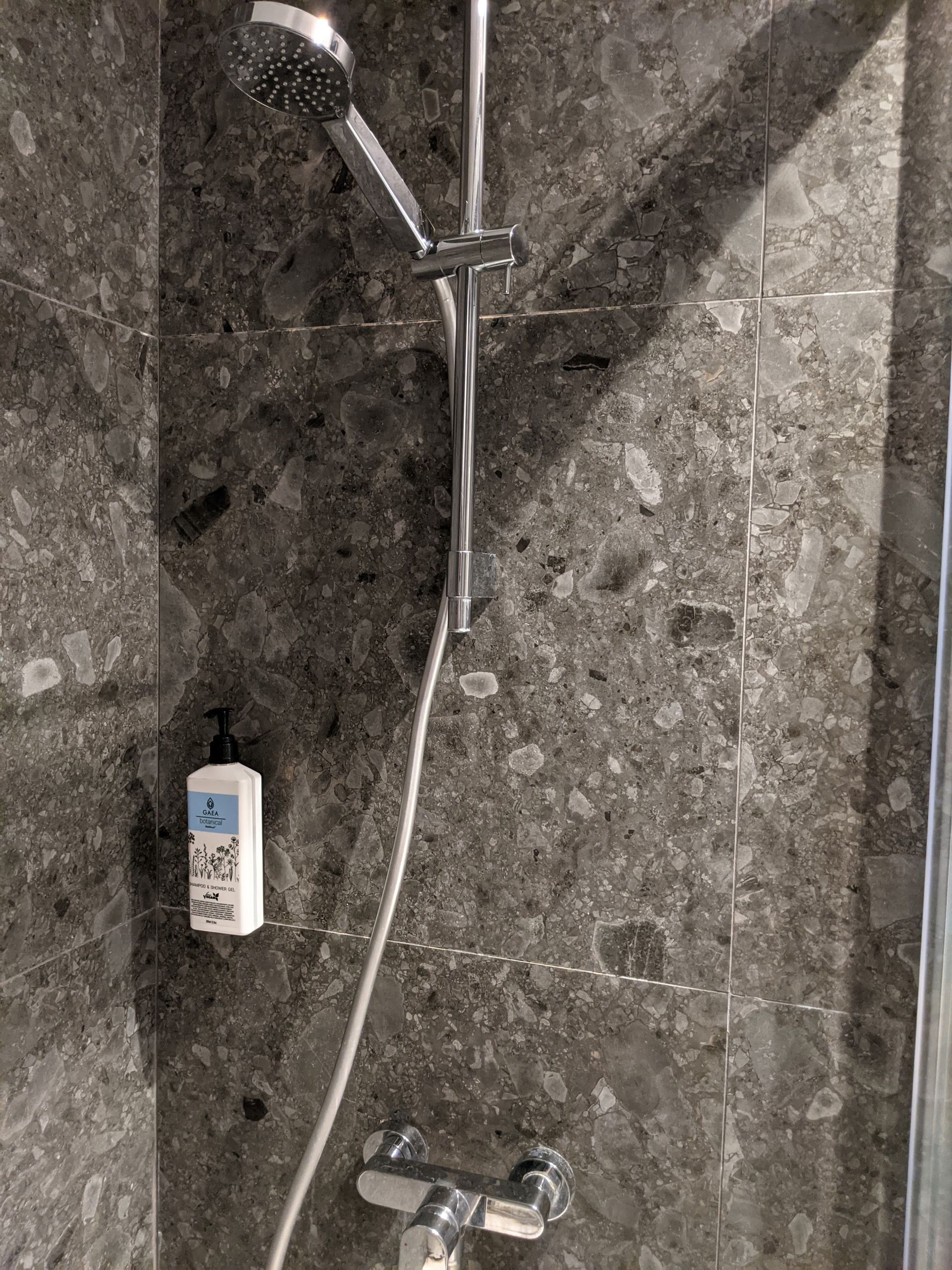 Shower stall with dark gray stone-like tiles, silver fixtures, and a white soap dispenser.