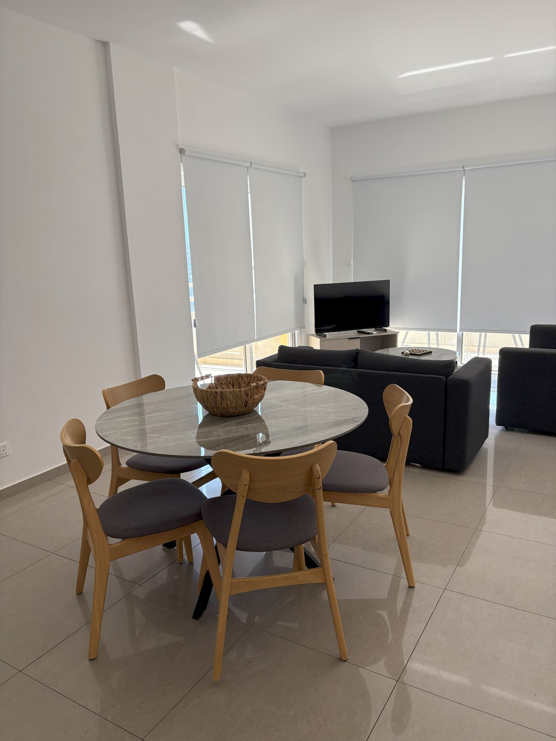 A modern dining area with a round table and six chairs, overlooking a balcony with city views.