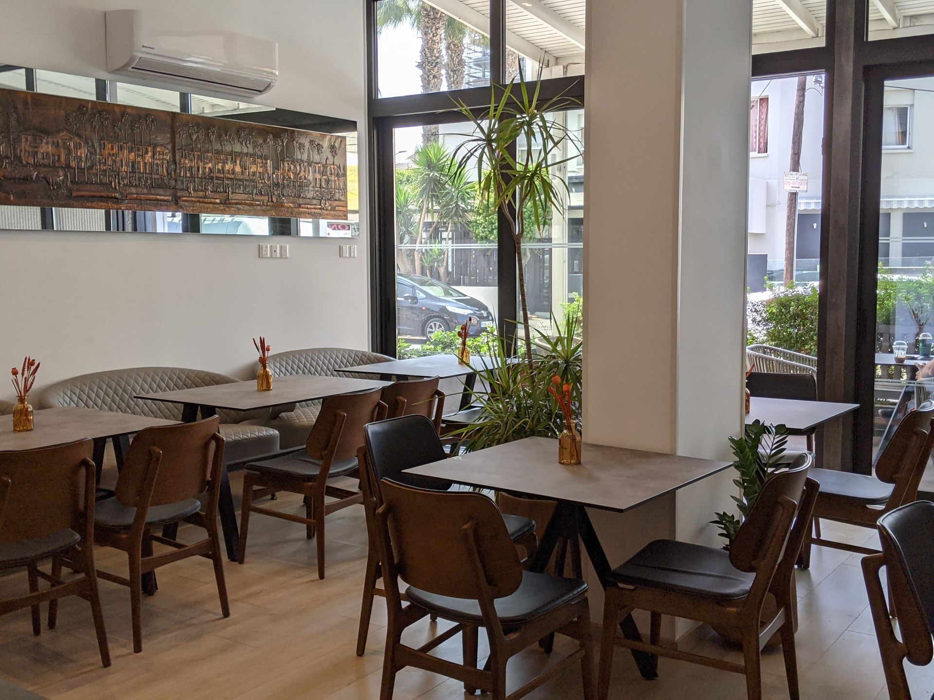 Interior of a cafe with wooden tables and chairs, a large window, and decorative plants.