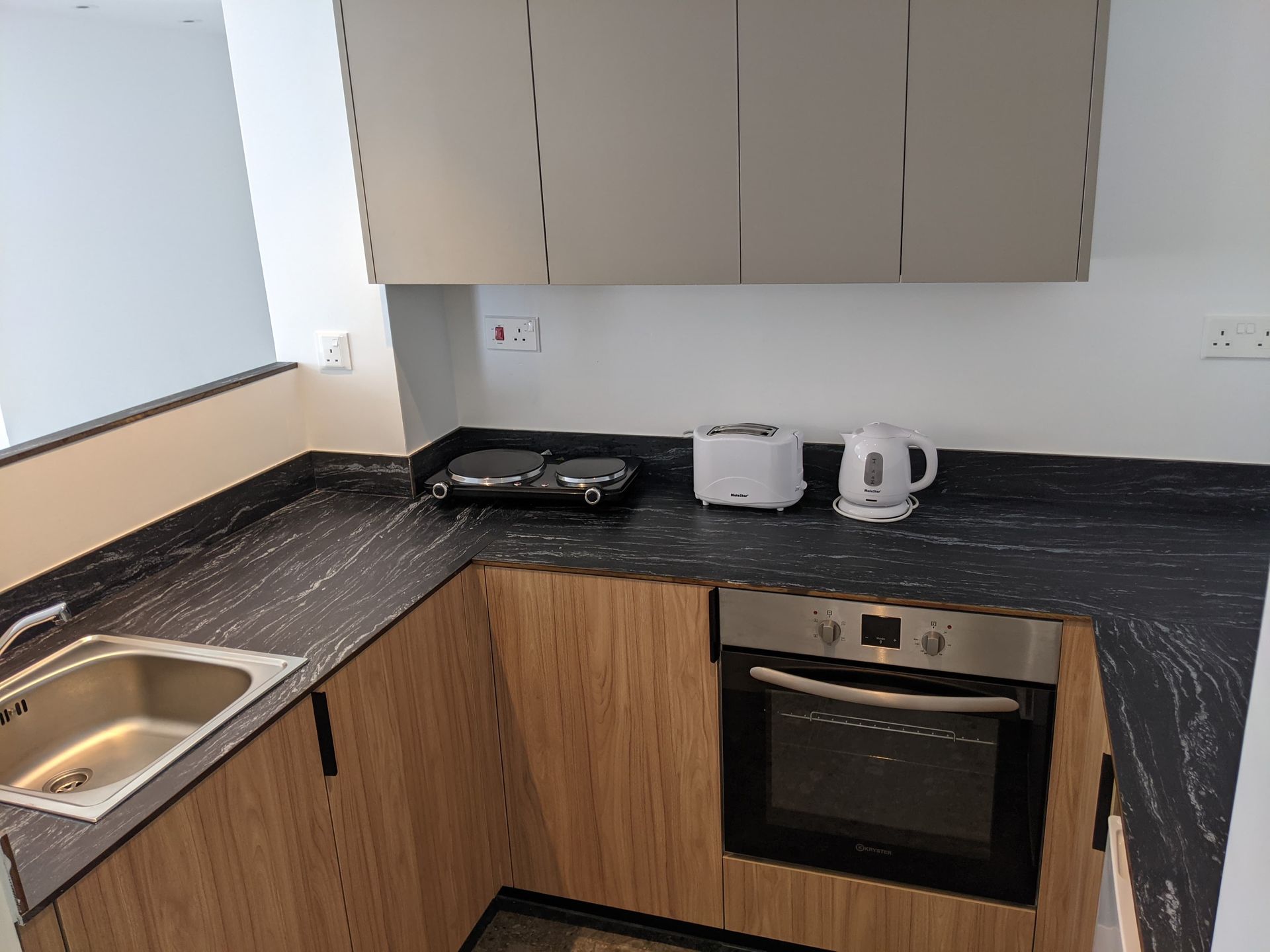 A kitchen with a sink , oven , toaster and kettle.