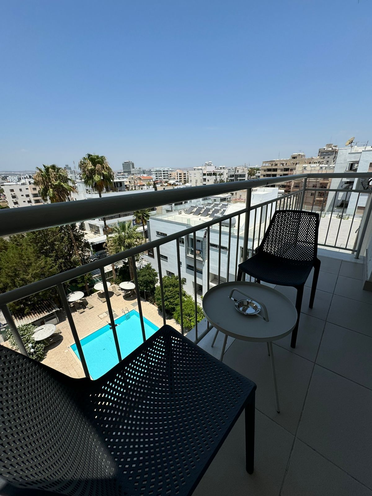 A balcony with a table and chairs overlooking a swimming pool.