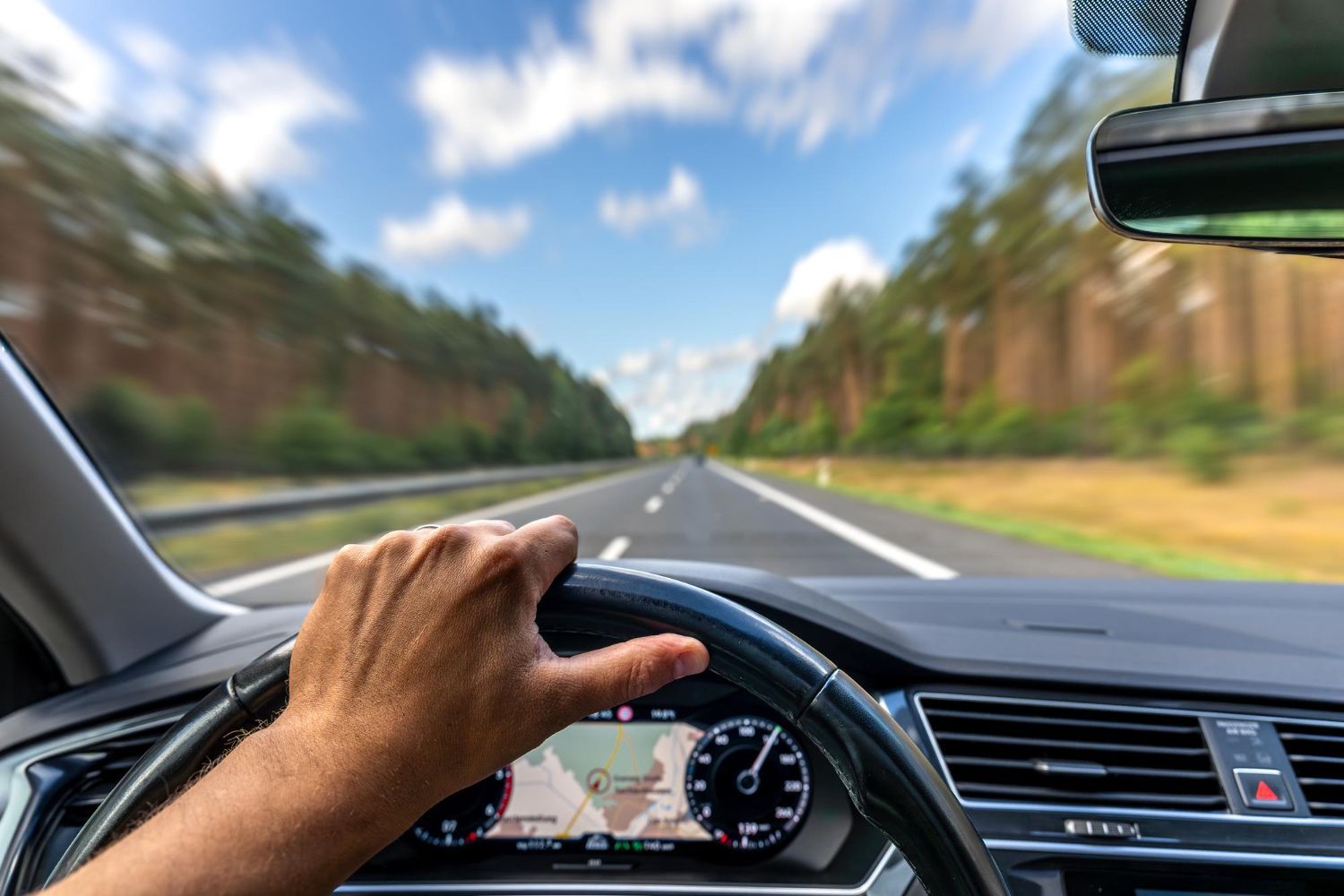 Hand on steering wheel, driving on highway with blurred background.