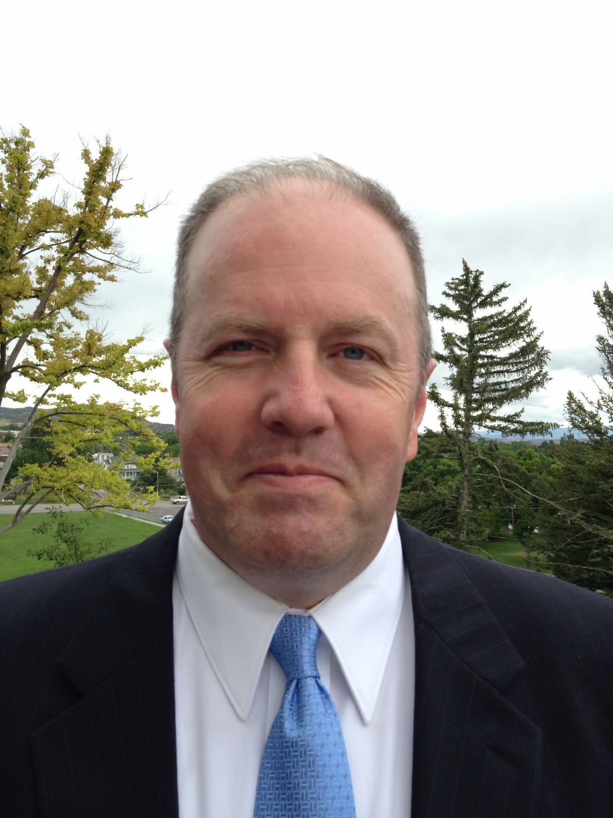 Man wearing a green and white plaid shirt smiles at the camera.