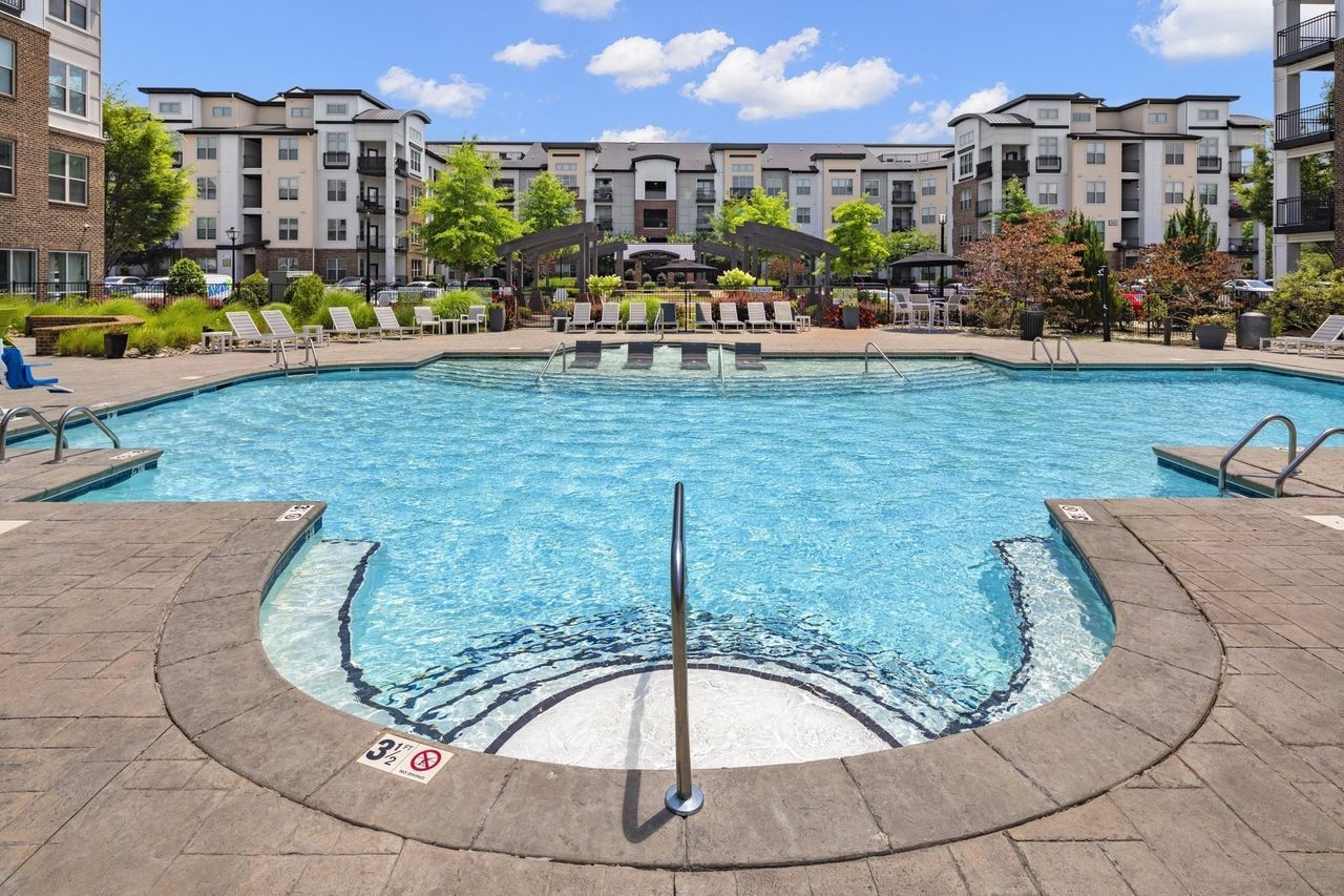 A large swimming pool with a hot tub in the middle of it in front of a building.