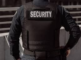 A security guard is wearing a black vest with the word security on it.