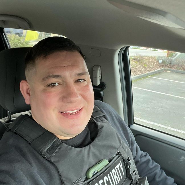A man wearing a security vest is sitting in the back seat of a car.