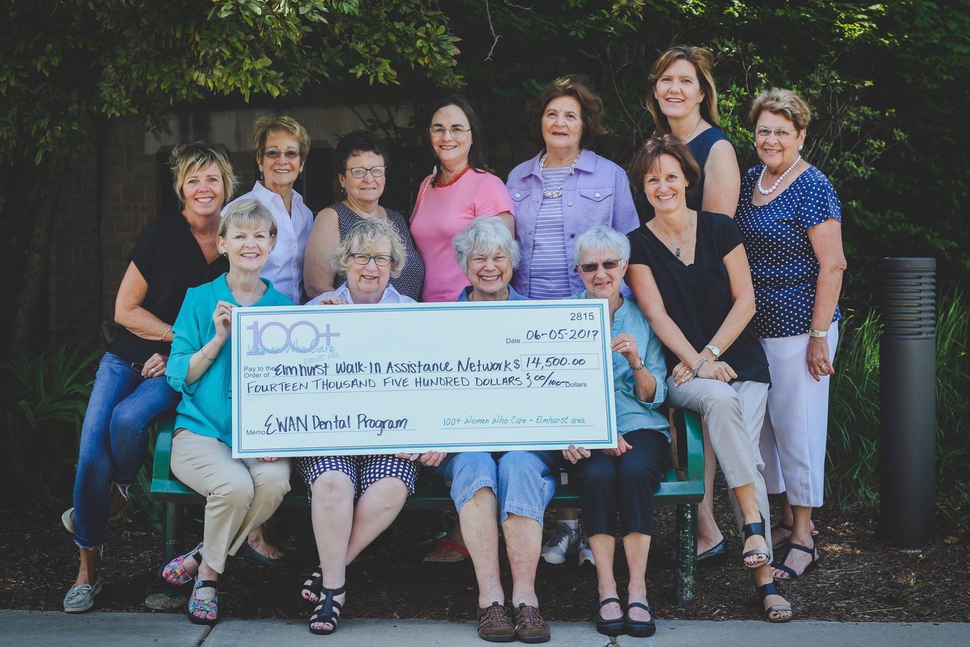 A group of women sitting on a bench holding a large check
